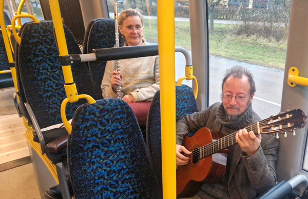 Kvinna med tvärflöjt och man med gitarr sitter ner i bussen.