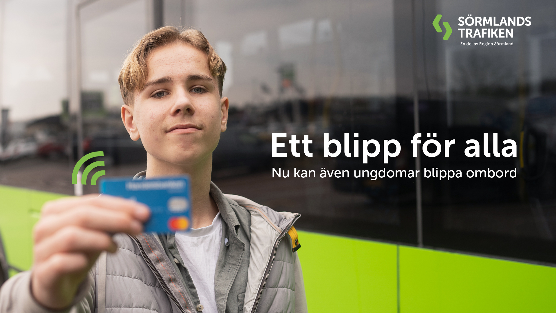 Bilden föreställer en ung resenär som håller upp sitt bankkort med en av Sörmlandstrafikens bussar i bakgrunden. 